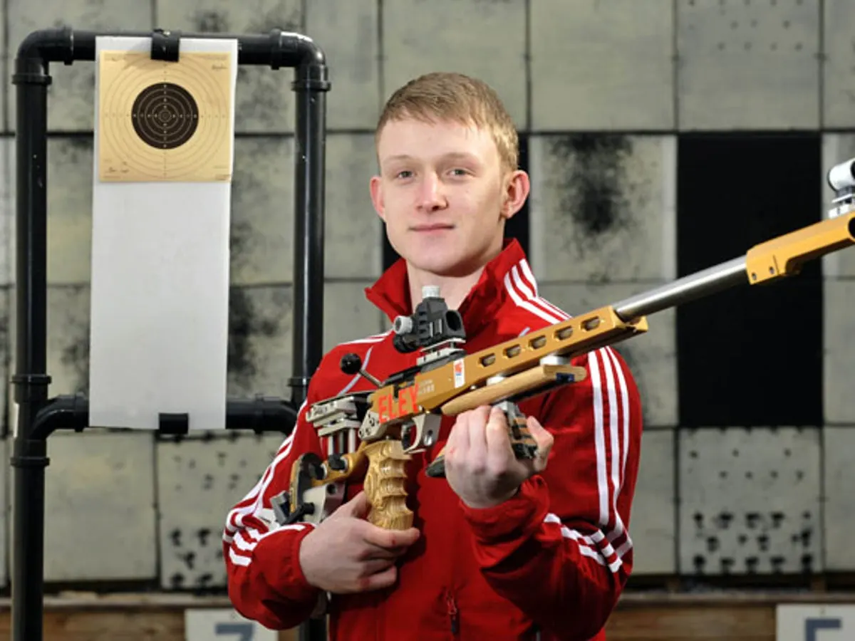 James Huckle holding a competition rifle at an indoor shooting range